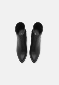 Bottines en cuir noir avec un bout pointu et une fermeture éclair, présentant une texture lisse et un design élégant et épuré.