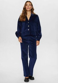 Marine modra žametna obleka z odprto jakno z velikimi gumbi in napihnjenimi rokavi, v kombinaciji z ujemajočimi se ravnimi hlačami.