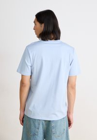 Light blue cotton t-shirt with short sleeves, a crew neck, and a smooth texture. The fit is relaxed, shown from the back.