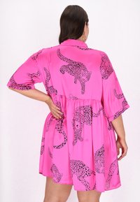 Różowa sukienka z gładkiego materiału, z zabawnym czarnym wzorem w panterkę. Luźny krój z krótkimi rękawami i marszczonym detalem w talii.