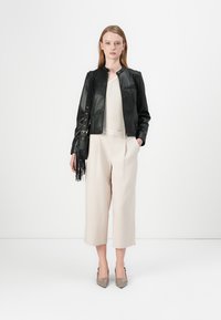Giubbotto bomber in pelle nera, top in maglia beige, pantaloni a gamba larga color crema e décolleté grigi a punta. Accessorio: borsa a tracolla piccola con frange.
