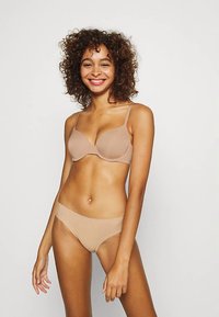 Sujetador nude ligero y ropa interior bikini a juego, textura suave, tirantes finos, diseño sin costuras y cobertura mínima.