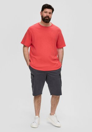 Rode T-shirt met korte mouwen en een ronde hals, gecombineerd met donkergrijze cargoshorts. Witte sneakers maken de outfit compleet.