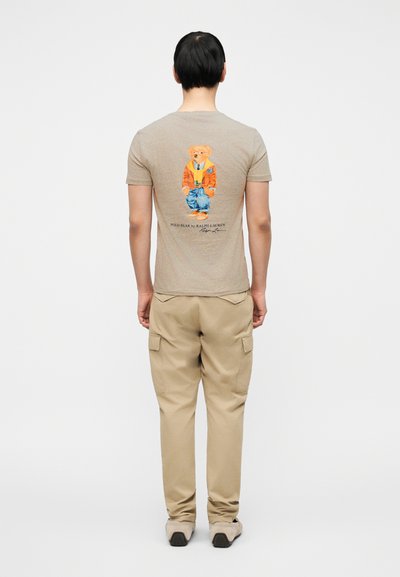 Μπεζ βαμβακερό μπλουζάκι με πολύχρωμο γραφικό μιας αρκούδας με σακάκι και τζιν πίσω. Συνδυασμένο με μπεζ cargo παντελόνια.
