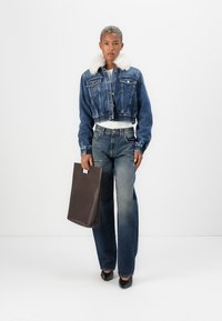 Chaqueta de mezclilla recortada con cuello de peluche sintético, jeans azules y un bolso tote marrón. Zapatos de tacón negros completan el conjunto.