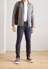 Kostkovaná bunda v námořnické modři a žluté, bílé tričko, námořnické kalhoty a černé tenisky. Obsahuje kabelku přes rameno a jemné detaily na zipu.