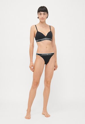 Melna krūštura un tanga komplekts ar V-veida dizainu, regulējamiem siksniņām un zīmola elastīgām joslām ar baltu tekstu. Gluda auduma tekstūra.