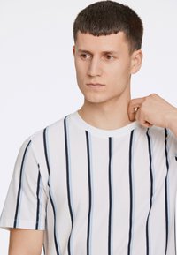 Vit kortärmad t-shirt med vertikala marinblå och ljusblå ränder, rund halsringning och mjuk bomullstextur.