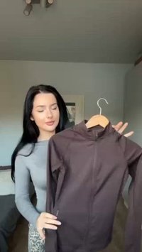 Tamno smeđi zip-up jakna s visokim ovratnikom, glatke teksture i prilagođenim dizajnom. Ima bočne džepove i duge rukave.