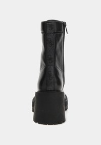 Botín negro de cuero hasta el tobillo con plataforma gruesa, cremallera trasera y lengüeta de tela vertical en un fondo blanco.