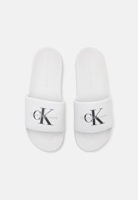 Infradito bianche con un cinturino in tessuto che presenta un prominente logo nero "CK" e il testo "Calvin Klein Jeans". Design soffice e leggero.