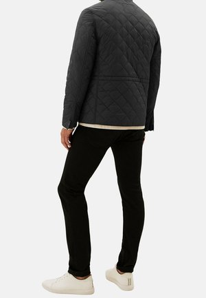 Černá prošívaná bunda s stojacím límcem a vzorem diamantů, v kombinaci s úzkými černými kalhotami a bílými teniskami.