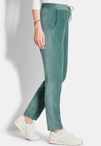 Groene corduroy joggers met een trekkoord in de taille, zijzakken en taps toelopende pijpen, gecombineerd met witte sneakers voor een casual uitstraling.