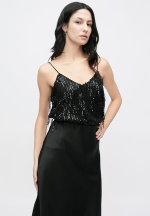 Crni top s šljokicama i resama, upareni s elegantnom crnom satenskom suknjom. Uske naramenice na topu ističu V-izrez. Ukupno glatka tekstura.