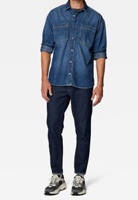 Denim overhemd met twee borstzakken, blauwe kleur, met knoopsluiting. Gecombineerd met donkere jeans en sneakers met een dikke zool.