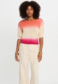 Gebreid top met een gradient van licht koraal naar diep rozenpink, korte mouwen en een ronde halslijn, gecombineerd met beige wijde broekspijpen.