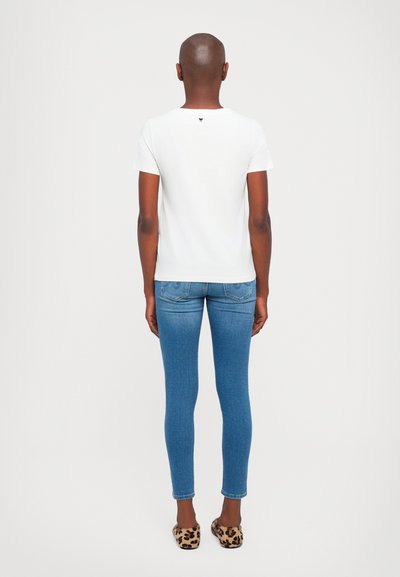 T-shirt bianco a maniche corte con scollatura rotonda, jeans skinny blu e ballerine con stampa leopardata. Vista posteriore semplice che mostra il dettaglio del logo sulla maglietta.
