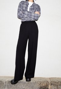 Rutigt knapp-up skjorta i mörkblått och vitt, tillsammans med svarta videbyxor och svarta träskor med silvernitar.