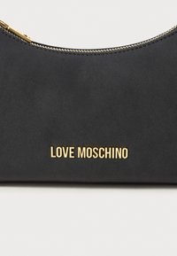 Black suede half-moon bag with gold zipper and "LOVE MOSCHINO" gold metal logo on front against a white background.