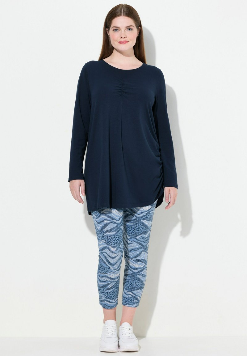 Maglietta a maniche lunghe color navy con ruching frontale abbinata a leggings chiari a pois con stampe di onde e animali. Sneakers bianche completano il look.