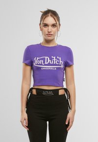 Violets krāsas īss krekls ar balto "Von Dutch Originals" logo. Mīksta kokvilnas auduma, īsas piedurknes, apaļa kakla izgriezums. Kombinēts ar melniem augstās jostasvietas biksēm.