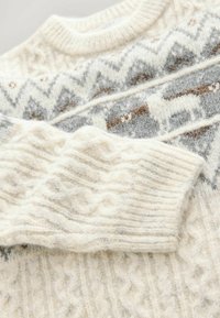 Knit sweater in cream, featuring gray and brown geometric patterns and reindeer motifs. Has ribbed cuffs and a textured cable design.