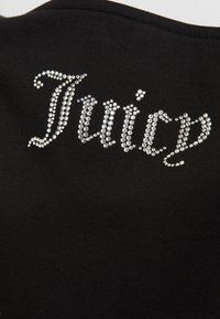 Črn top iz blaga z napisom "Juicy" iz kamenčkov, z teksturirano površino in okroglim izrezom, ki poudarja bleščeče podrobnosti.