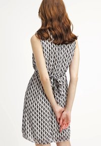 Svart- och vitmönstrad ärmlös klänning med knytning i midjan, tillverkad i ett lätt och smidigt material. Klänningen är av medellång längd och har en avslappnad passform.
