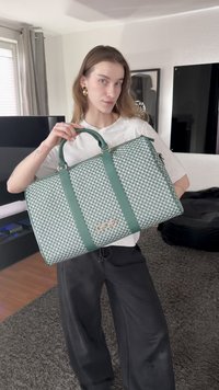 Zaļa rakstaina rokassomiņa ar diviem rokturiem, rāvējslēdzēja aizdari un zelta logotipa akcentu. Teksturēta virsma ar ģeometrisku dizainu.