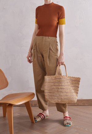 Hnědý žebrovaný top s krátkým rukávem se žlutými akcenty, béžové plisované kalhoty, slamá taška a vícebarevné pruhované sandály.