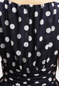 Marineblaues Kleid mit großen weißen Punkten, ausgestattet mit gerafftem Rücken und Taillengummi, glattem Stoff und einem verdeckten Reißverschluss.