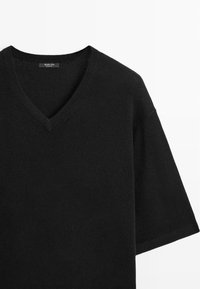 Black V-neck sweater in a soft, knitted texture with short sleeves. Simple design features a seamless neckline and relaxed fit.