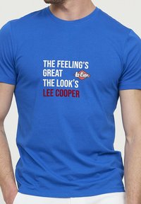 T-shirt en coton bleu avec un texte audacieux en blanc et rouge : "LA SENSATION EST GÉNIALE, LE LOOK EST LEE COOPER." Design classique à col rond.