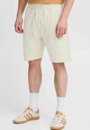 Cremefarvede bomuldsshorts med elastisk talje og snor. Sammenstylet med hvide sokker og beige sneakers. Enkel og afslappet design.