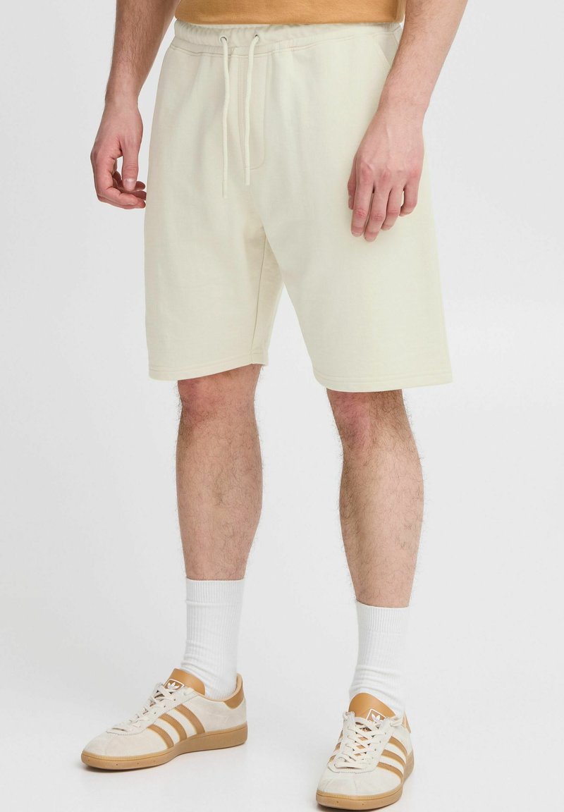 Shorts en coton de couleur crème avec une taille élastique et un cordon de serrage. Associés à des chaussettes blanches et des baskets beiges. Design simple et décontracté.
