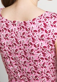 Květinové šaty v růžové barvě se vzorem listů v bílé a červené. Mají kulatý výstřih a zapínání na zip na zádech. Bavlněná látka.