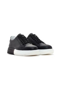 Des sneakers en cuir noir présentent un dessus lisse, un design à lacets, une semelle en caoutchouc blanche et un subtil accent texturé sur le talon.