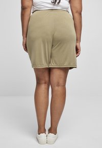 Khaki shorts med elastisk midjebånd, myk tekstur og avslappet passform. Synlige sømdetaljer langs kantene. Et par hvite sko.