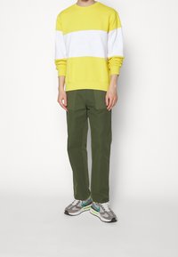 Gul och vit färgblockerad sweatshirt med relieftryckt logga, tillsammans med olivgröna raka byxor. Grå och gröna sneakers fulländar looken.