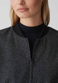 Schwarze Bomberjacke aus strukturiertem Stoff mit geripptem Kragen. Verfügt über einen Frontreißverschluss und einen kontrastierenden Strickunterlayer.