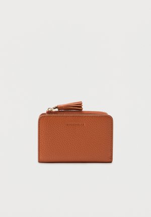 Hnědá texturovaná kožená peněženka se zipem a střapcem, kompaktní obdélníkový tvar, značka COCCINELLE vyražená na přední straně.