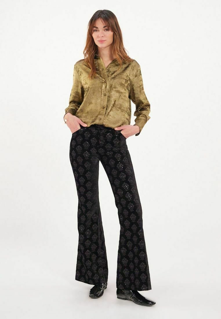 Blouse olive légèrement brillante à boutons ; pantalon noir évasé avec un motif texturé en paisley et des accents métalliques.
