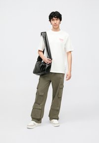 White t-shirt with red print, olive cargo pants with multiple pockets, and black shoulder bag. Completing with white sneakers. Simple design.
