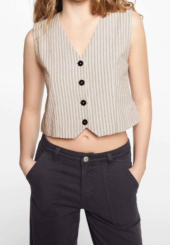 Béžové pruhované tílko bez rukávů s výstřihem do V a pěti černými knoflíky vpředu; nošené přes tmavé, těsné kalhoty.