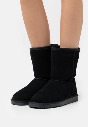 Botines de ante negro con un suave forro interior, suela de goma plana y diseño de punta redonda. Presentan costuras mínimas y sin adornos.