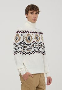 Biały sweter z golfem wykonany z dzianiny, ozdobiony geometrycznym wzorem w odcieniach brązu, czerni i burgundowego na klatce piersiowej oraz rękawach.