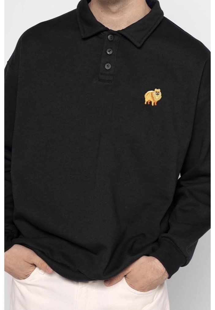 Svart långärmad pikétröja med treknapplist, med en broderad gul hunddesign på vänster bröst. Slät struktur.