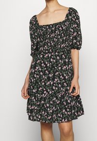 Schwarzes Blumenkleid mit kurzen puffärmel, quadratischem Ausschnitt und gestuftem Rüschensaum. Enthält kleine rosa und grüne Blumenmuster im gesamten Kleid.
