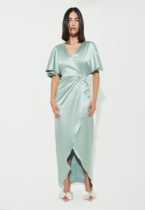Mintgrøn satin kjole med en indhyllet design, korte flæseærmer og en høj slits. Samlet med lyse mule-sko med sløjfe-accent.