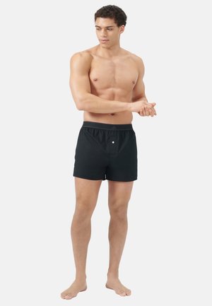 Zwarte zwemshorts van lichtgewicht stof, met een elastische tailleband en een enkele knoop aan de voorkant. Gladde textuur met een getailleerde pasvorm.